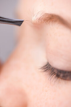 Extreme close up of young woman plucking own eyebrow hair with tweezers
