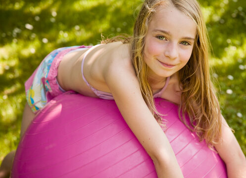 Portrait of young blonde girl lying on pink ball smiling
