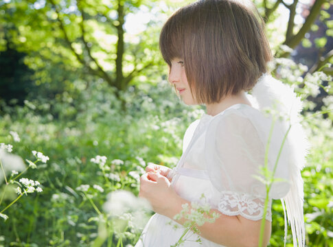 Portrait of young girl in a white fairy costume standing in a garden
