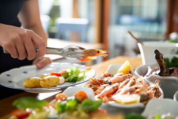 A restaurant customer puts delicious shrimp on a plate. Seafood buffet lunch in a cafe