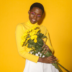 cheerful African American woman model with yellow flowers in yellow clothing on a yellow background