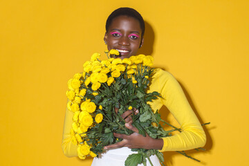 smiling African American woman model with yellow flowers in yellow clothing on a yellow background