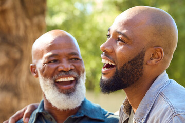 Portrait Of Laughing Senior Father With Adult Son Standing Outdoors In Garden Park Or Countryside