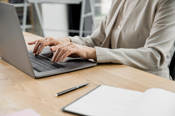 Fototapeta premium partial view of businesswoman typing on laptop near pen and notebook on work desk in office