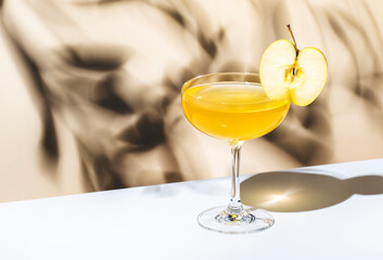 Apple pie cocktail drink with vodka, apple liqueur and cinnamon syrup.. Light beige background, hard light, shadow pattern
