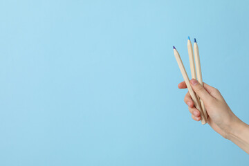 Female hand holds multi-colored pencils on a blue background, place for text