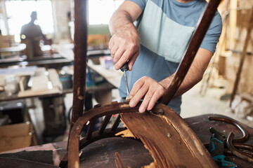 Close up of male craftsman in furniture restoration workshop fixing old wooden chair, copy space