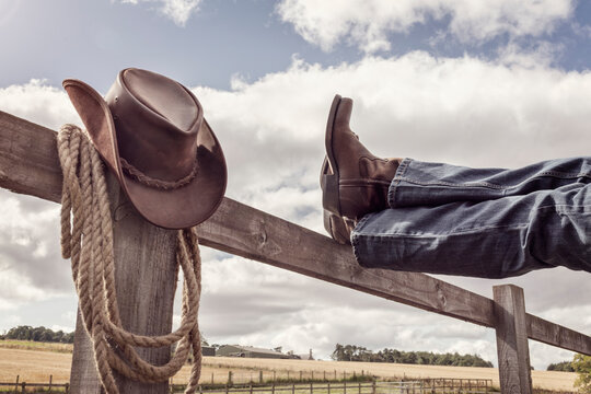 Cowboy boots and hat with feet up on fence resting with legs crossed