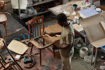 High angle portrait of black male craftsman fixing old furniture in workshop, copy space