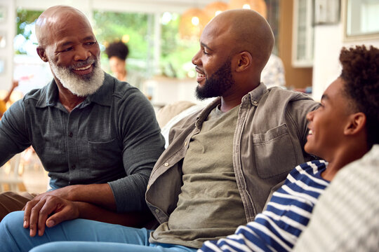 Laughing Multi-Generation Male Family Hanging Out On Sofa At Home Talking Together