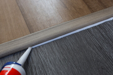 Silicone sealant. Applying silicone caulking on wood floor.