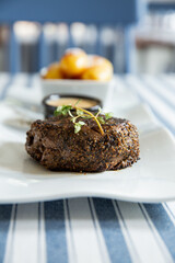 Appetizing medium rare grilled beef steak with baked potato and sauce served on white plate.
