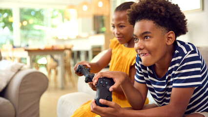 Brother And Sister Sitting On Sofa At Home Playing Video Game Together  © Monkey Business