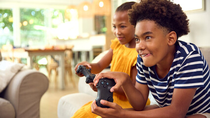 Brother And Sister Sitting On Sofa At Home Playing Video Game Together 