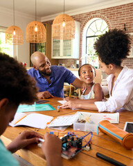 Family Around Table At Home Using Laptop With Parents Helping Children With Science Homework