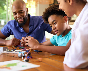 Fototapeta premium Family Around Table At Home Using Laptop With Parents Helping Son With Science Homework