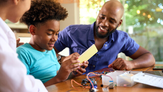 Family Around Table At Home Using Laptop With Parents Helping Son With Science Homework