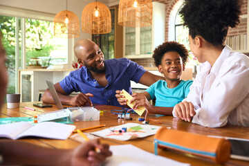 Family Around Table At Home Using Laptop With Parents Helping Children With Science Homework