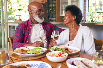Loving Senior Couple Sitting Around Table At Home Enjoying Meal With Wine Together
