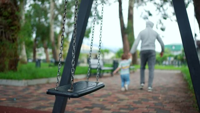 a kidnaper and a child on the playground on the background of a swing