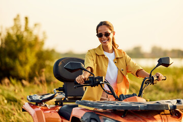 Fototapeta premium Portrait of a smiling woman driving a rented quad bike, with sunglasses on.
