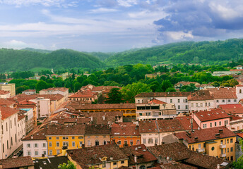 Fototapeta na wymiar travel summer view from hill to a nice european town with amazing buildings, green hills and mountains with amazing cloudy evening sky on background