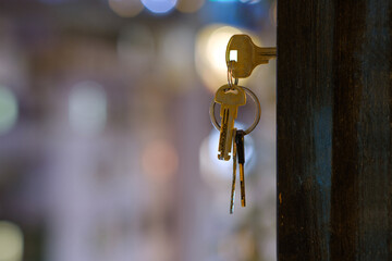 The keys with key ring in the door keyhole with blurred night lights background, selective focus
