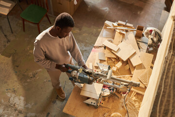 High angle portrait of young black man as carpenter cutting wood in sunlit workshop, copy space