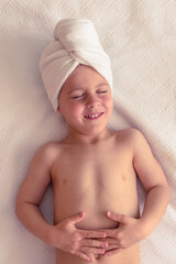 Smiling boy with towel on head resting on bed