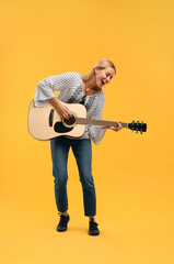 Happy hippie woman playing guitar on yellow background