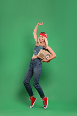 Happy hippie woman with retro radio receiver dancing on green background