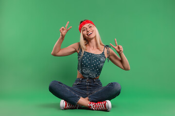 Portrait of happy hippie woman showing peace signs on green background