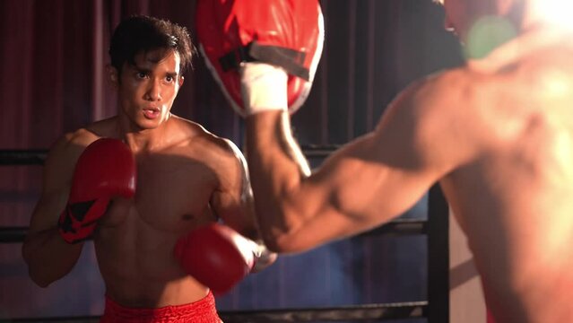 Asian and Caucasian Muay Thai boxer unleash punch in fierce boxing training session, delivering punching strike to sparring trainer, showcasing Muay Thai boxing technique and skill. Impetus