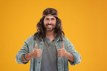 Stylish hippie man showing thumbs up on orange background