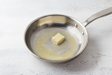 A piece of butter is melted in a frying pan on a light gray background. Making cheese pasta sauce, step by step, do it yourself, step 1