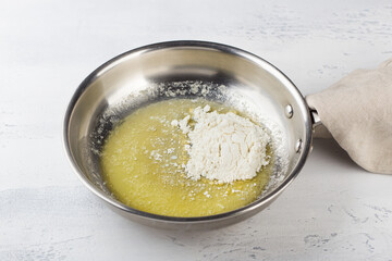 Flour is added to melted butter in a frying pan on a light gray background. Making cheese pasta sauce, step by step, do it yourself, step 2 - 642049373