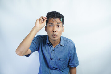 Confused Asian young man take off glasses, look with puzzled and displeased face, cringe from something strange and awful, standing in blue shirt against white background