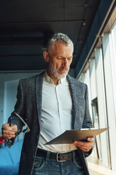 Focused businessman looking on documents and think how to solve problem while standing in office