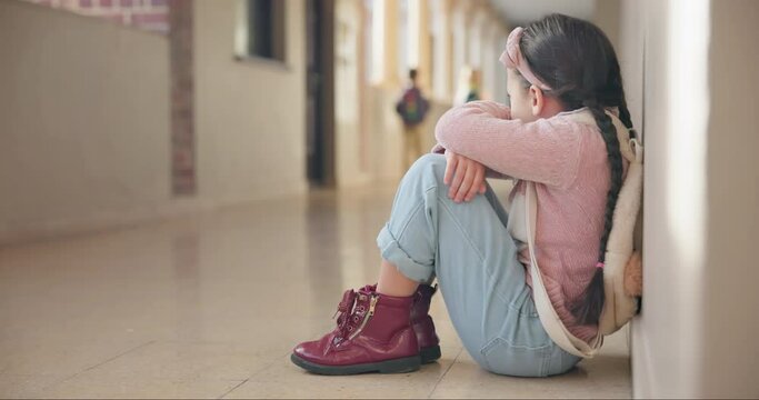 Scared, loney and a child in a school corridor for bullying, autism or sad about education. Mental health, anxiety and a student or girl sitting in a hallway of kindergarten with fear for learning