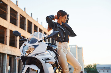 Building behind. Woman is with motorcycle outdoors