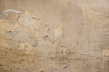 Old brown paint with cracks and chips on the uneven surface of a concrete wall. Texture