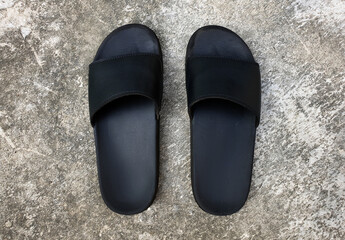 A pair of old black slip-on slippers sandals on grey concrete floor. Basic pair of open toe slide...