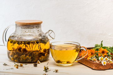 Freshly brewed chamomile flower tea in a glass teapot, a cup of tea and chamomile and calendula...
