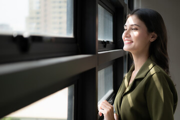 Portrait of a beautiful young woman standing near the window and smiling