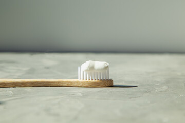 Natural bamboo toothbrush with toothpaste on a gray background.