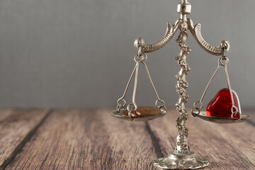 Antique scales of justice with red heart shape and coins on wooden table. Copy space. Close-up....