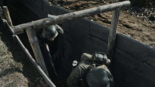 High angle shot of Nazi soldiers wearing helmet holding rifles cautiously moving along frontline trench, Second World War reenactment