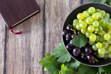 Fresh grapes in a bowl with green vine leaves and holy bible book on wooden table. Top view....