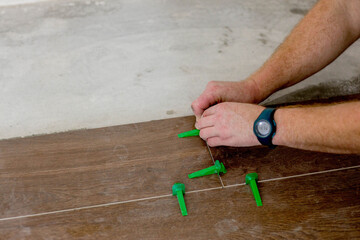 Close up hands of repairman laying tiles with tile leveling system on the floor in a new house