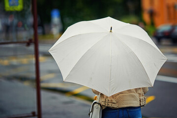 Woman with white umbrella waiting public transport on bus stop in rainy day. Selective focus